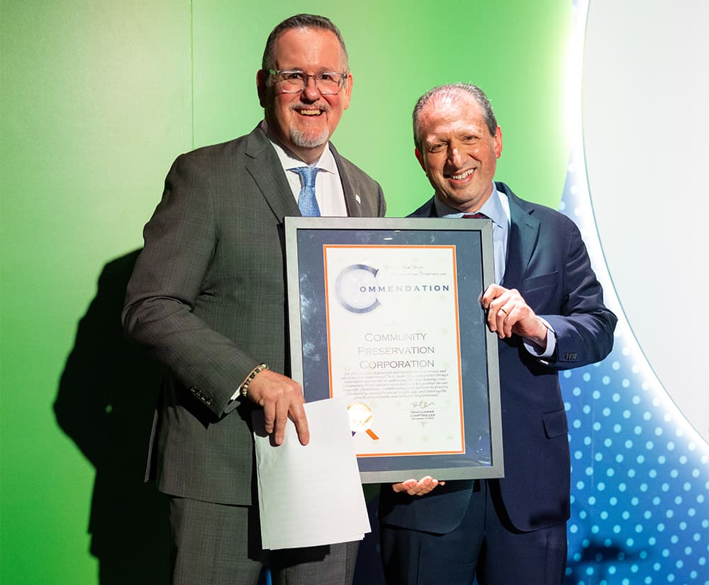 Two people smiling hold commendation plaque.